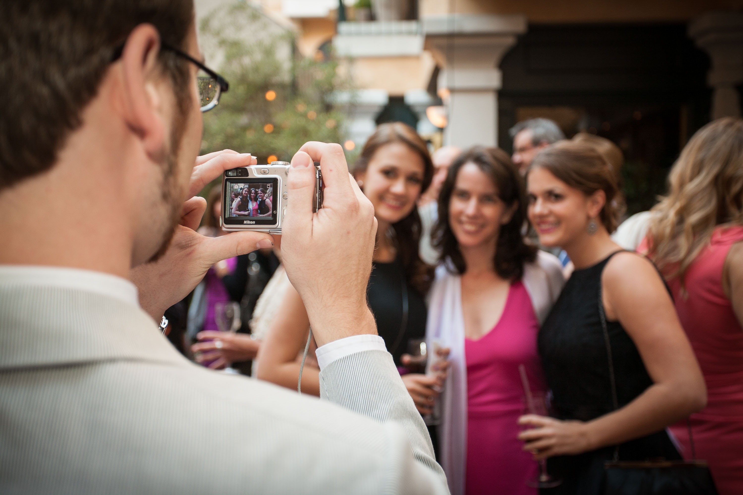 A man takes a snapshot of three pretty girls with a point-and-shoot camera  at the Garden Court Hotel in Palo Alto