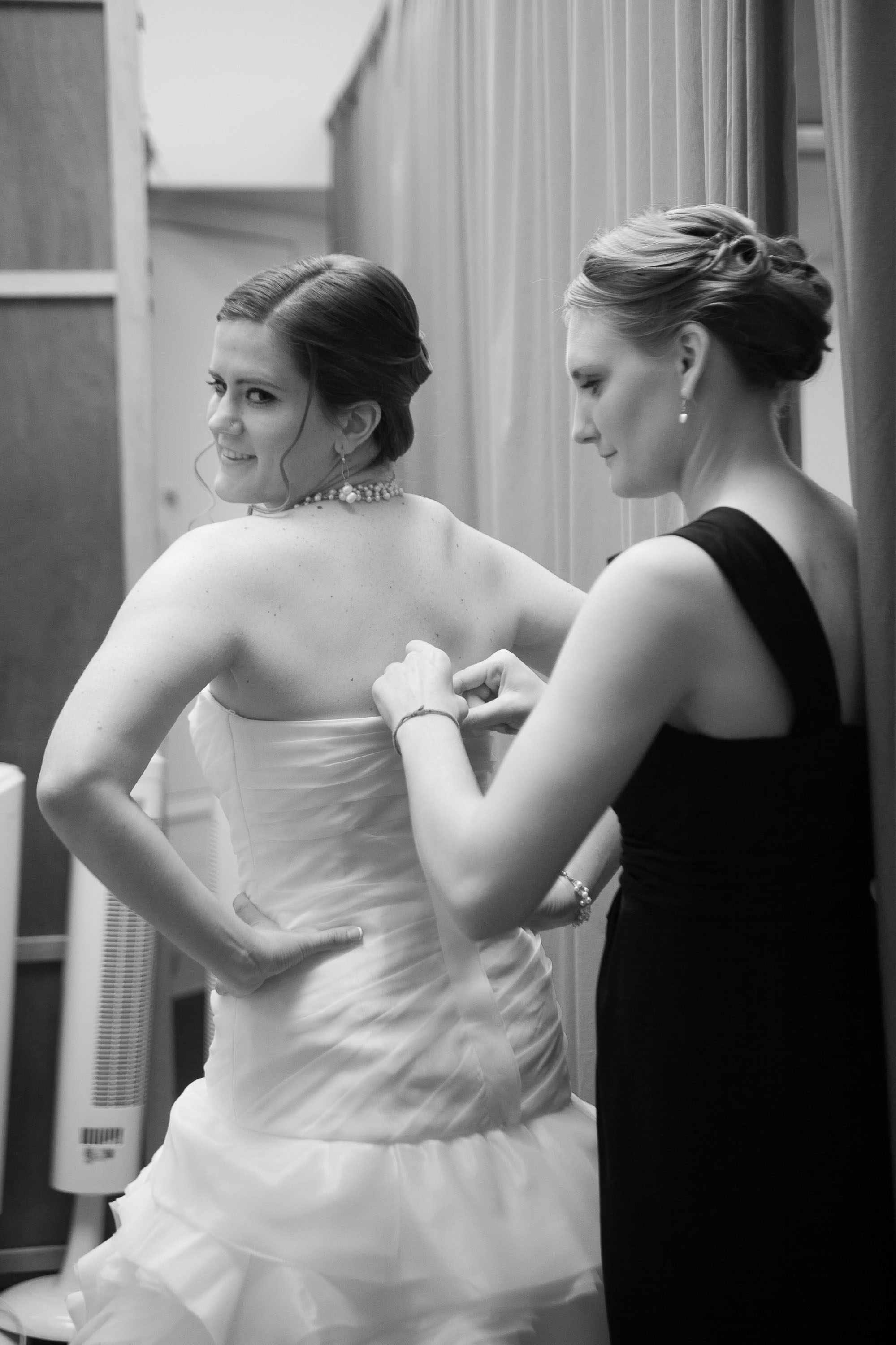 The bride glances back as her bridesmaid puts the finishing touch on her Vera Wang gown, at Pema Osel Ling in the Santa Cruz mountains