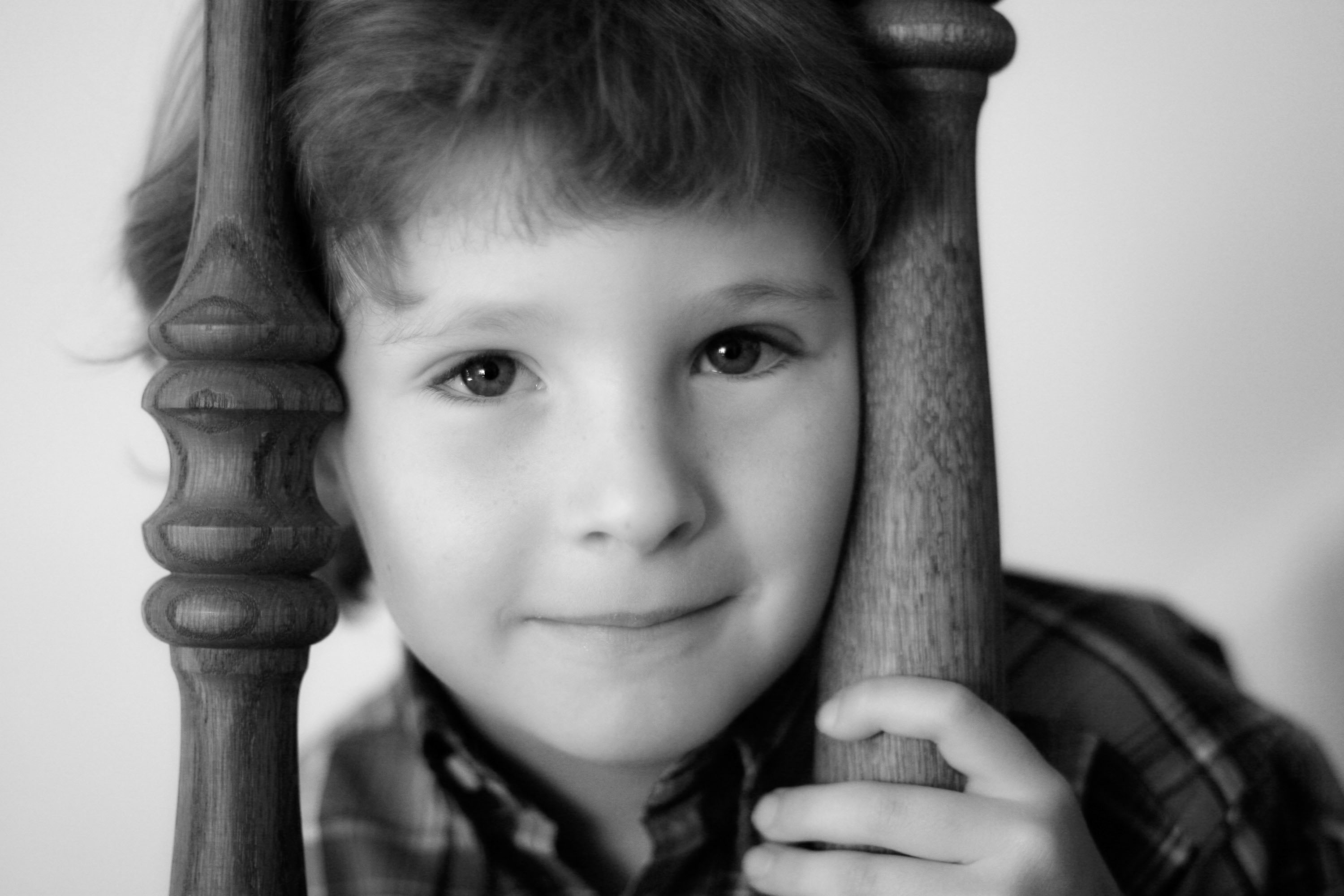 A young boy with beautiful eyes peeks through a banister in a thoughtful portrait from Checkerbox Photography.