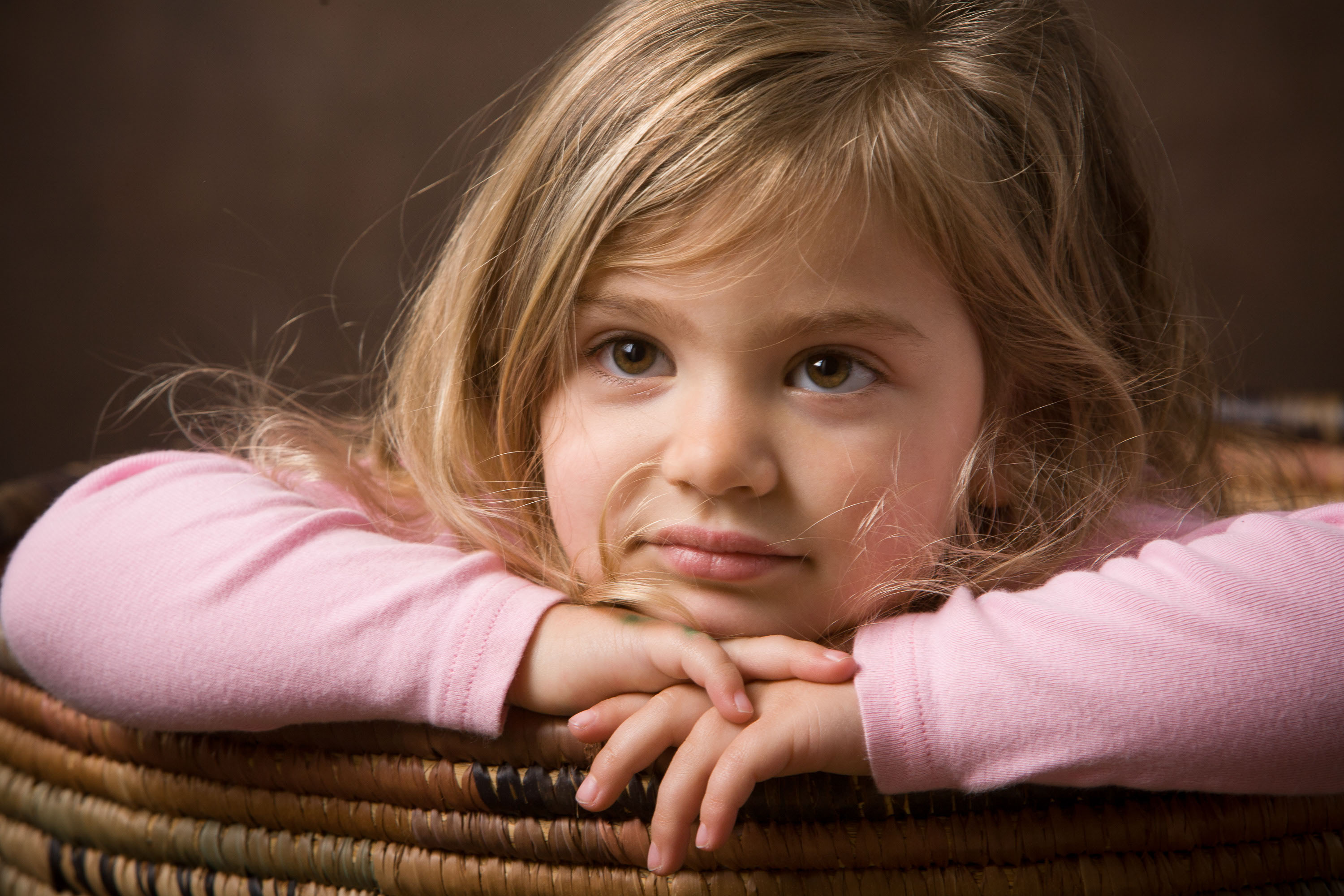 A pensive young lady pokes her head out ouf a basket in a sensitive studio portrait.