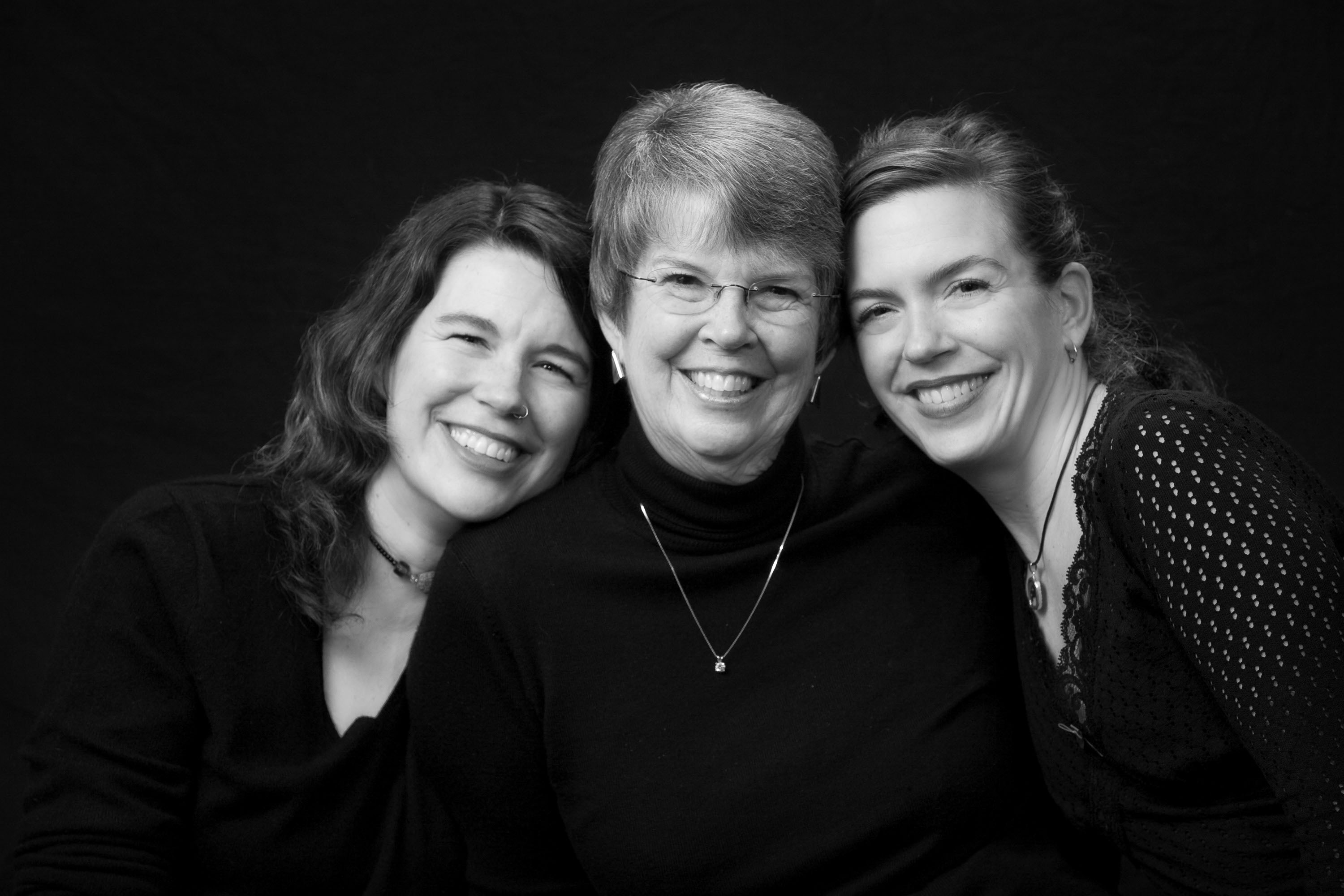 A mom and her two grown daughters in a classic black and white studio portrait.