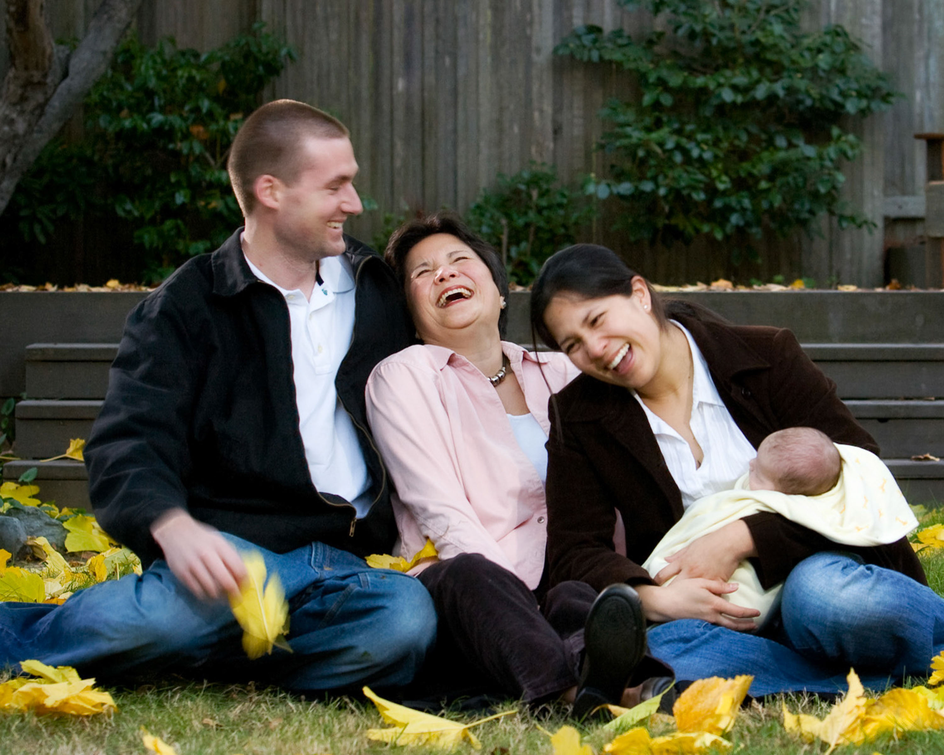 A Berkeley family laughing in the Fall leaves in their backyard.