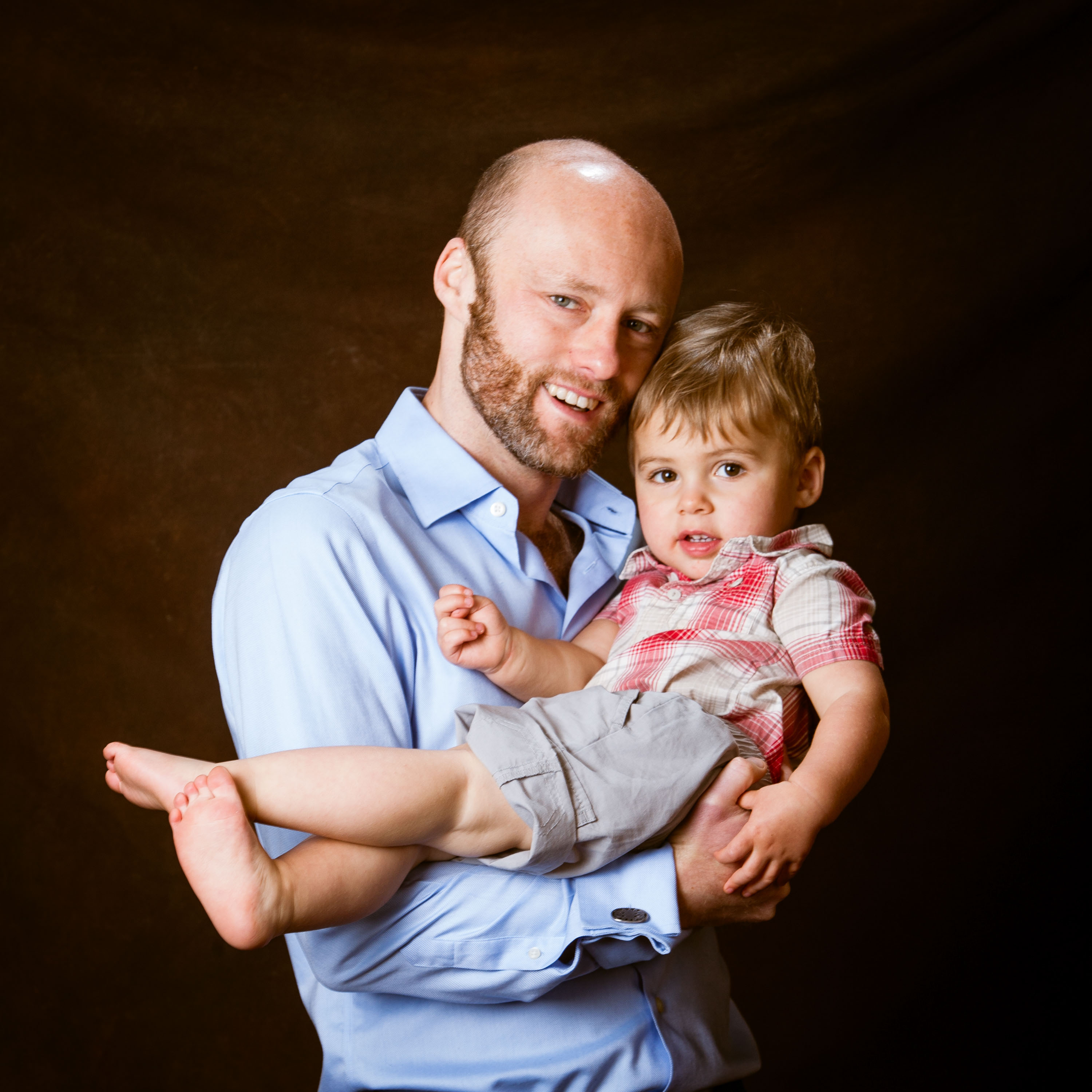 A dad holds his barefoot son in a beautiful family portrait made in the studio.